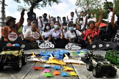 Thai university students raise a three-finger salute in front of toys representing the powerful military during a protest in Bangkok
