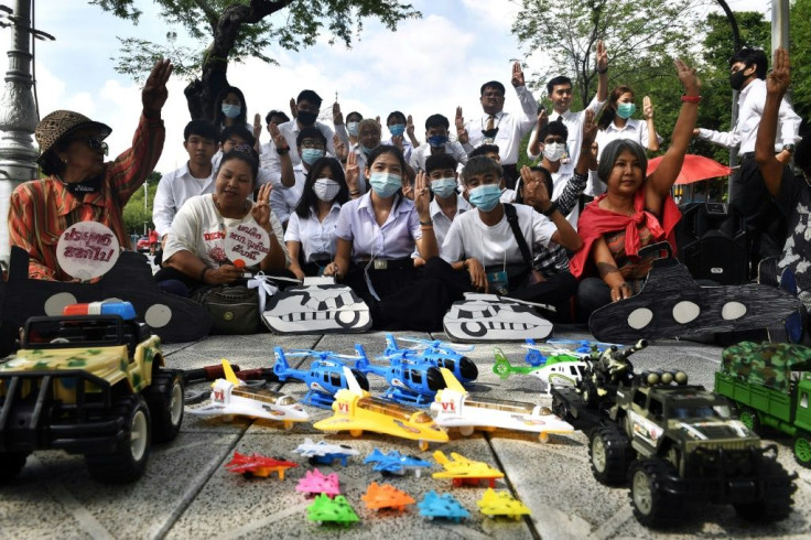 Thai university students raise a three-finger salute in front of toys representing the powerful military during a protest in Bangkok