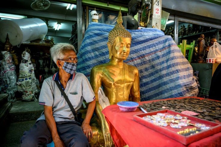 A vendor wearing a face mask against the spread of the coronavirus sits beside a Buddha statue as he waits for customers at an amulet market in Bangkok