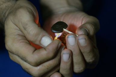 A Pakistani smoker holding a match to a clump of hashish to soften it before mixing it with cigarette tobacco