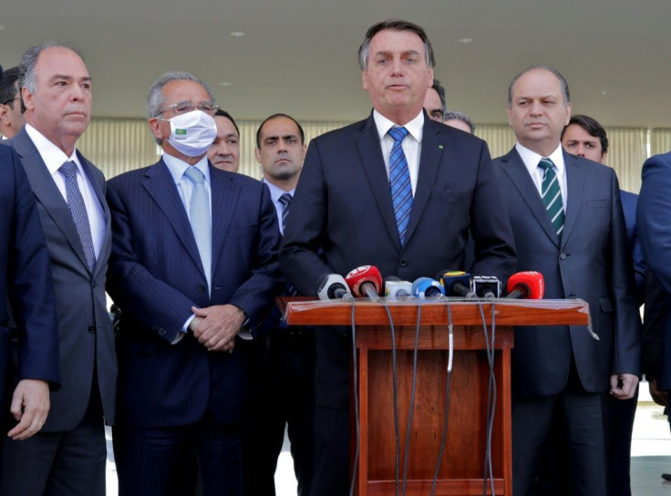 Brazilian President Jair Bolsonaro (C) speaks alongside Brazilian Economy Minister Paulo Guedes (L), deputies and senators during a statement on financial aid for vulnerable Brazilians amid the COVID-19 pandemic, at Planalto Palace, in Brasilia