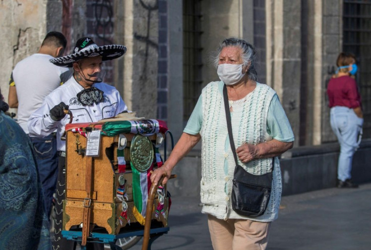 A woman with a face mask walks past a man wearing traditional Mexican attire and a face shield as he plays the organ in Mexico City ahead of the Independence Day celebrations.