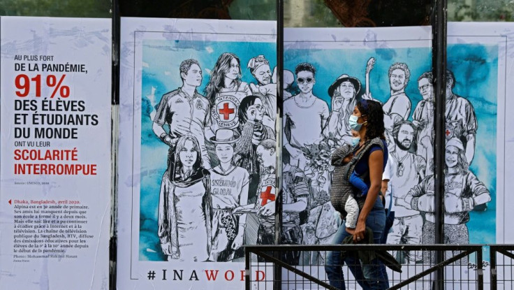 A woman with her baby walks past a street art poster created by the French artist Combo for the  International Committee of the Red Cross in Paris