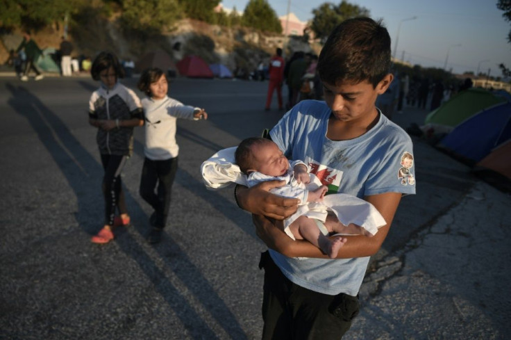 A boy carries his newborn brother after sleeping on a main road at the island of Lesbos