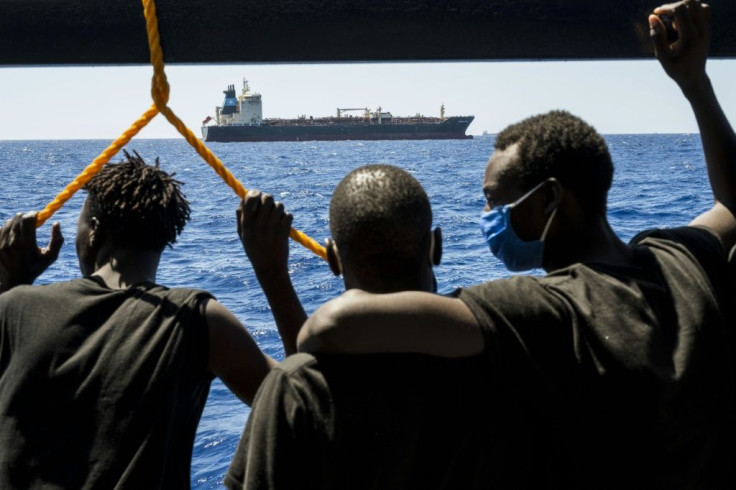 Migrants onboard a different ship in the Mediterranean look at the Maersk Etienne freighter on August 27