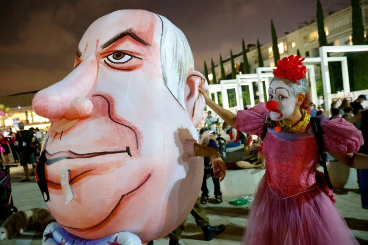 An Israeli woman in a clown's outfit mocks a giant caricature of Prime Minister Benjamin Netanyahu at a protest in Tel Aviv against the second lockdown