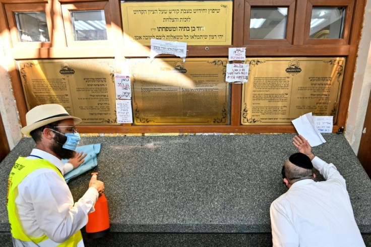 A worshipper stands ready to wipe the tomb of Rabbi Nahman with disinfectant as others kiss it
