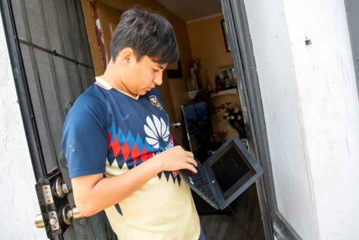 Angel, 13, stands outside his home trying to connect his computer to the wifi hotspot provided by a parked van from JFK company in order to follow his online classes in Santa Ana, California
