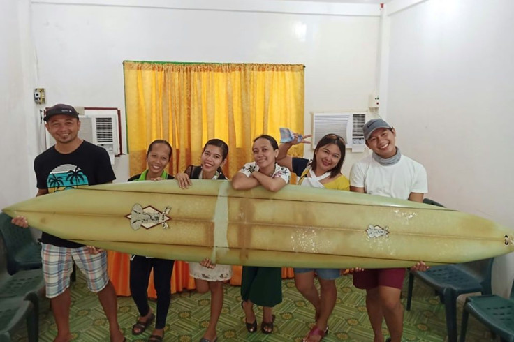 Filipino teacher Giovanne Branzuela (L) poses with the surfboard, once owned by big wave surfer Doug Falter who lost it while surfing in Hawaii two years