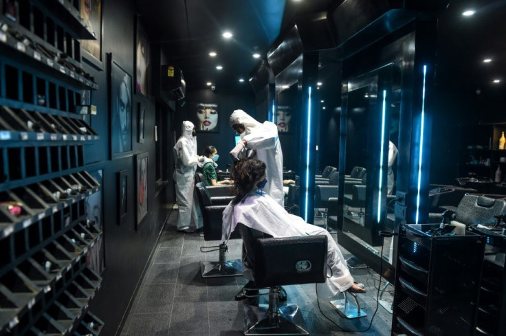 Hairdressers in protective suits attend to customers at a  hair and beauty salon in Ahmedabad, India