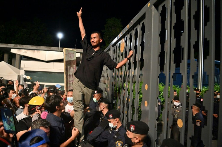 Activist Panupong 'Mike' Jadnok makes a three-finger salute to protesters after placing a 'People's Plaque' sticker on the main gate of Thailand's parliament during a pro-democracy rally