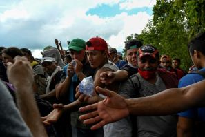 Honduran migrants, part of a caravan heading to the US, reach for water handed out by soldiers after crossing the border at Entre Rios, Guatemala on October 1, 2020
