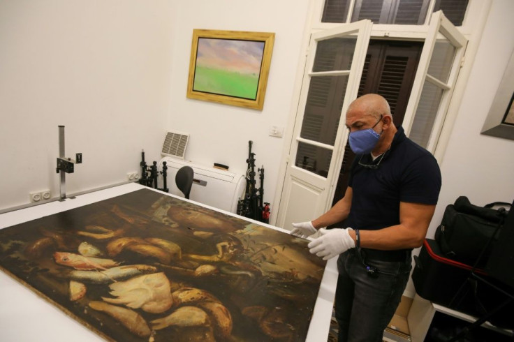 Gaby Maamary, a Lebanese artwork conservation specialist, examines a 17th-century painting by Italian painter Elena Recco, damaged in the Beirut port blast, at his studio in Beirut