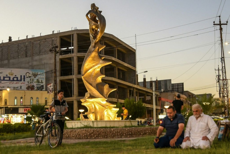 Men pray near the statue of 'My Lovely Lady' erected in the centre of a square in Iraq's northern city of Mosul