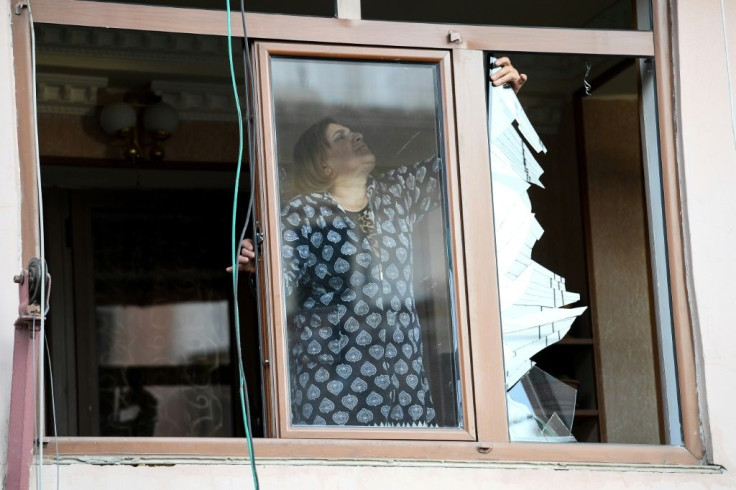 A woman removes broken glass from a window in an apartment building