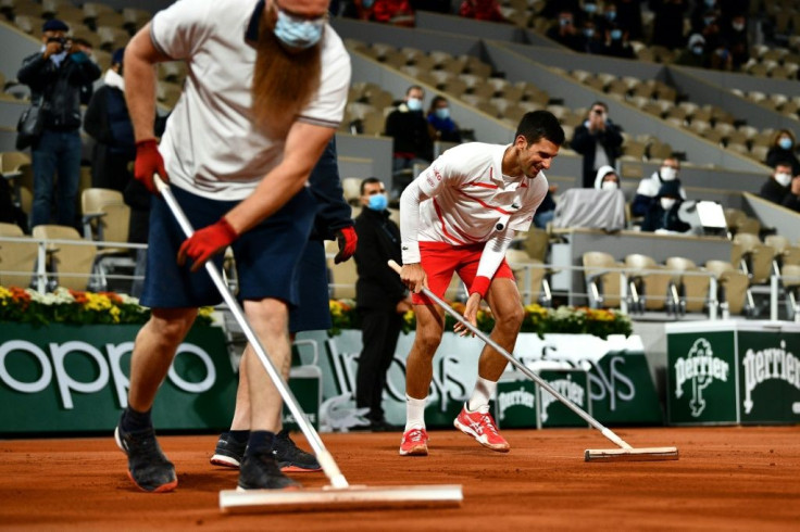 Sweeping to victory: Novak Djokovic helps groundstaff lay more clay to dry the surface after rain fell on Court Philippe Chatrier