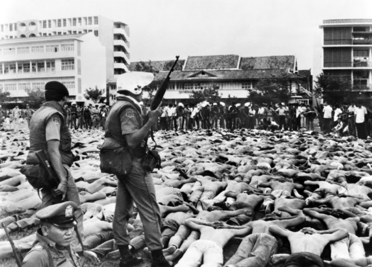 Shirtless students lie facedown on the ground, as police stand guard on the Thammasat University campus in Bangkok on October 6, 1976