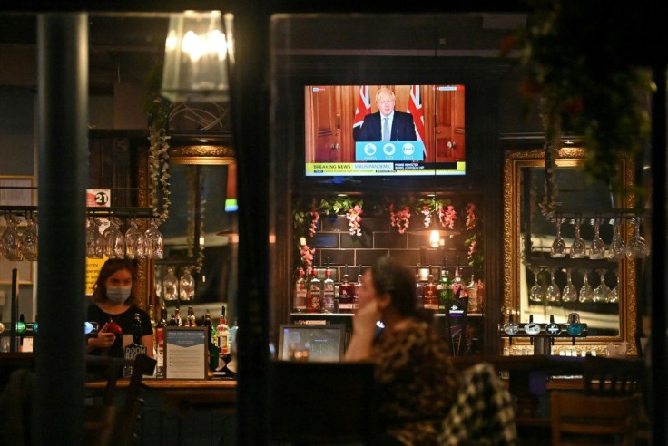 A television shows Britain's Prime Minister Boris Johnson addressing the country on new virus restrictions, as customers sit at the bar inside the William Gladstone pub in Liverpool