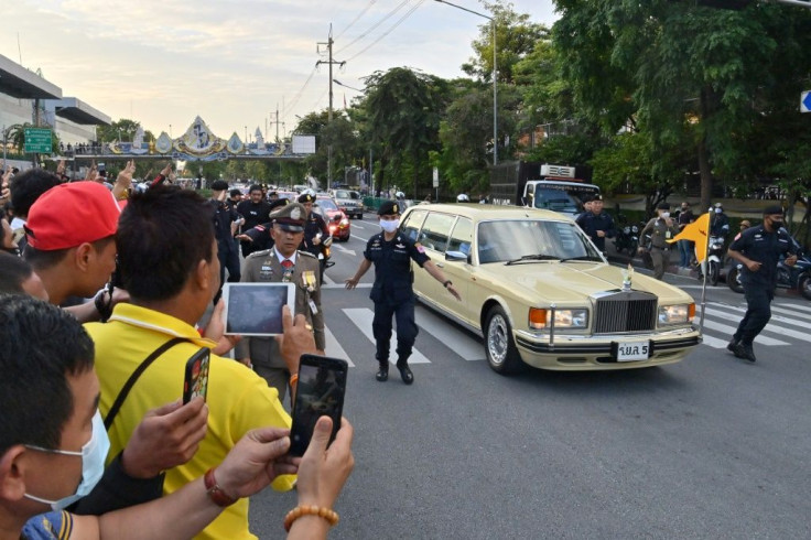 Some pro-democracy protesters give the three-finger salute beside royalist supporters as the limousine carrying Thailand's Queen Suthida and Prince Dipangkorn Rasmijoti passes in Bangkok on October 14