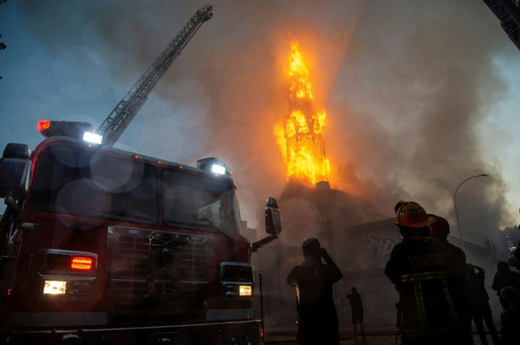 Firefighters work outside the burning church of Asuncion after it was set on fire by demonstrators in Santiago