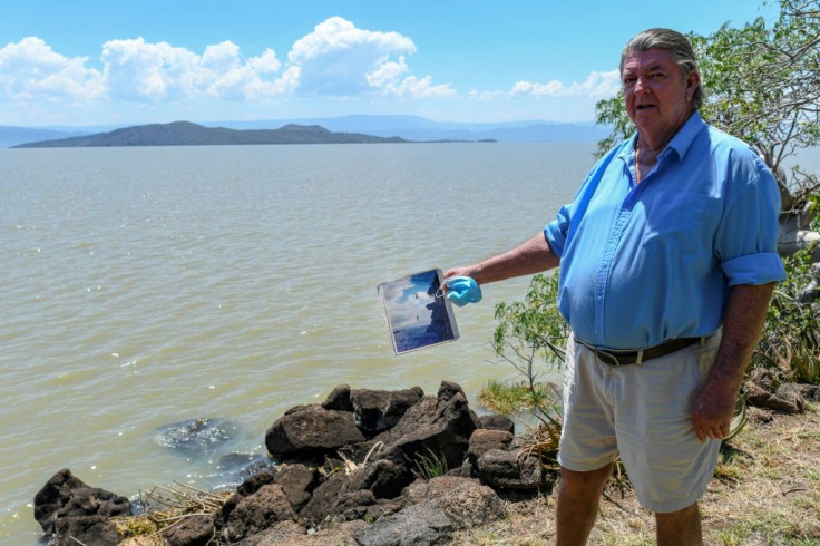 Murray Roberts, 69, holds an old photo of his sons jumping off a cliff face into the lake from the edge where he is standing that is now submerged