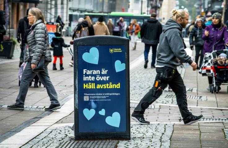 People walk past a trash can with a sign reading "The danger is not over - Keep your distance" in the Swedish city of Uppsala
