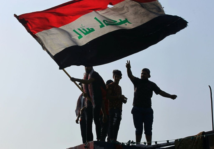 Iraqi demonstrators wave a flag as they gather in Tahrir Square in the centre of the capital Baghdad to mark the first anniversary of a movement demanding the ouster of the entire ruling class accused of corruption