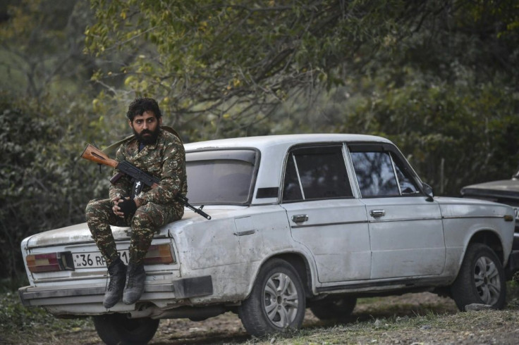A volunteer fighter sits on a car as cannons fire nearby