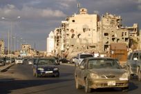 Cars drive near shell-pocked buildings in Libya's eastern coastal city of Benghazi on October 23, 2020, after a ceasefire agreement was signed between the country's warring factions