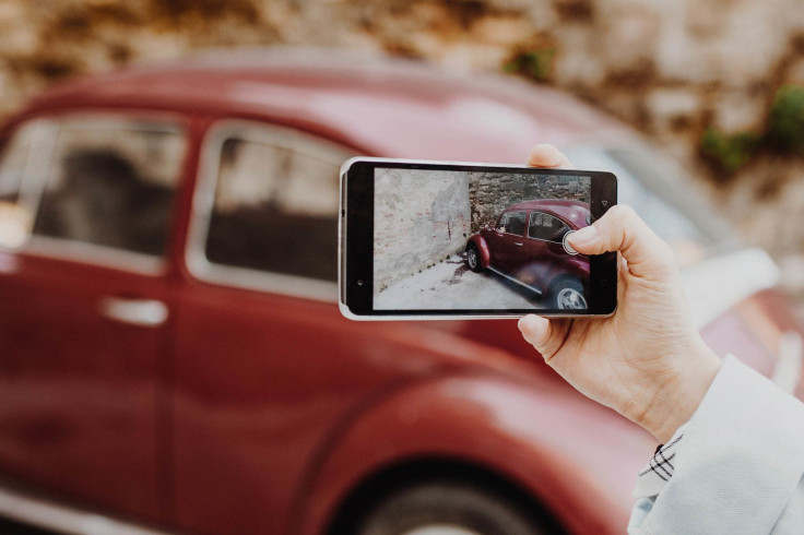 Girl taking photo of retro car with smartphone.