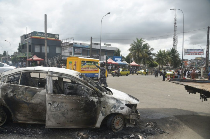 A policeman gestures next to a car in Abidjan's Cocody district that was torched in anti-Ouattara protests on October 19