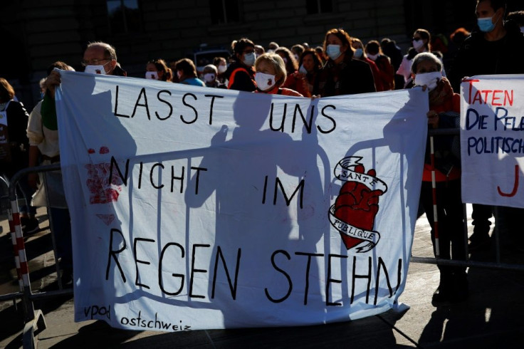 Healthcare workers wear protective face masks as they stand with a banner that reads in German. "Let us not stand in rain" during a demonstration in Bern, as part of a week of protests to call for higher salaries and better working conditions