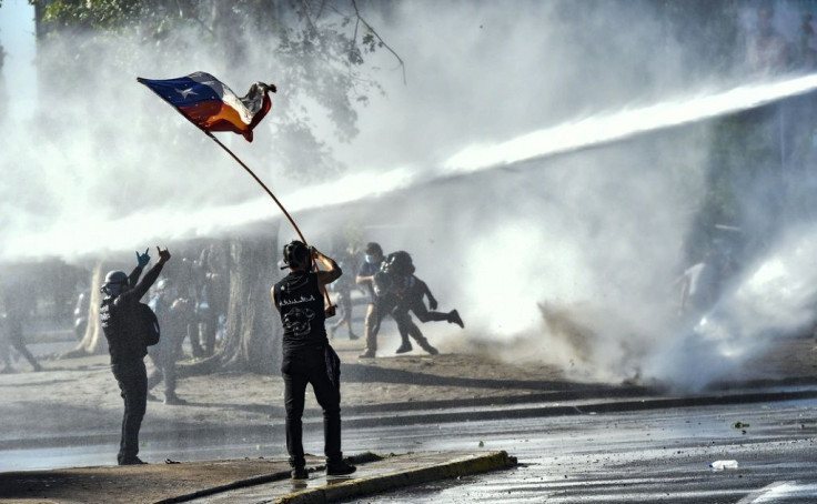 Demonstrators are sprayed by a riot police water cannon during a protest against Chilean President Sebastian Pinera's government in Santiago on October 30, 2020