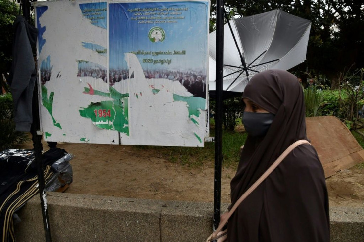 An Algerian woman walks past ripped posters calling on people to vote in a referendum for a new constitution, in the capital Algiers