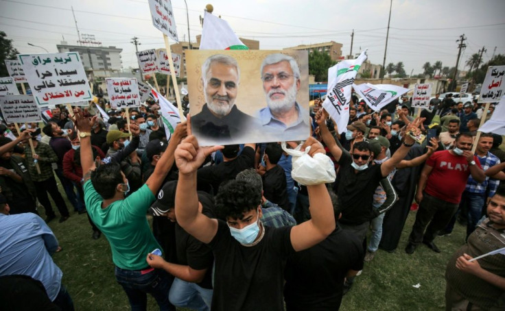 A protester holds aloft  portraits of (L to R) Iranian commander Qasem Soleimani and Iraqi paramilitary commander Abu Mahdi Al-Muhandis, both killed in a US drone strike in January