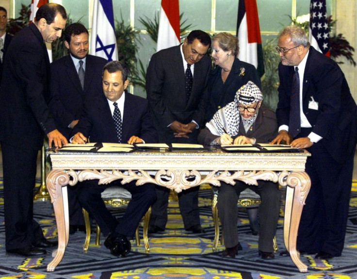 In this photo from September 4, 1999, Israeli Prime Minister Ehud Barak and Palestinian leader Yasser Arafat sign a landmark agreement paving the way for talks on a permanent peace settlement, as senior Palestinian negotiator Saeb Erakat (R) watches