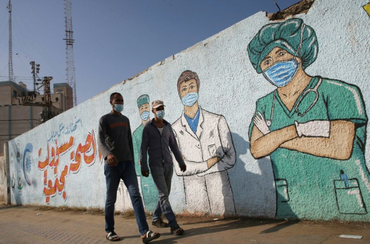 Palestinian men walk past street art showing doctors mask-clad due to the coronavirus pandemic, in Khan Yunis in the southern Gaza Strip