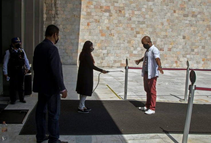 A worker sprays antibacterial liquid on a visitor at the entrance to the National Museum of Anthropology in Mexico City, on November 14, 2020, amid the COVID-19 coronavirus pandemic