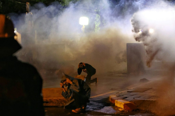 Pro-democracy protesters kneel down amid tear gas and water cannon fired by police during an anti-government rally in Bangkok on November 17, 2020