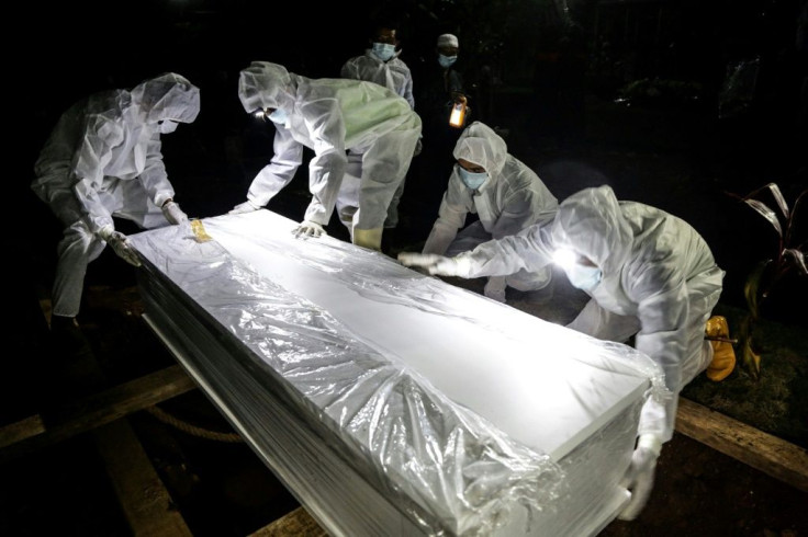 Graveyard workers in full prtective gear move a coffin in Bogor, Indonesia