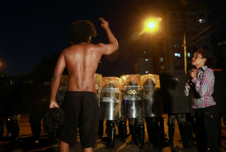 A man confronts riot police as a woman prays during a protest against the death of Joao Alberto Silveira Freitas in Porto Alegre, Brazil