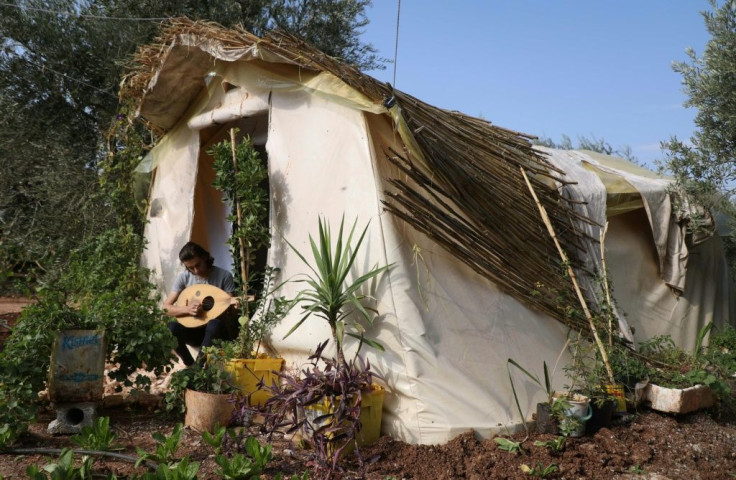 Displaced Syrian teenager Wissam Diab plays the oud at his new home, a tent surrounded by plants