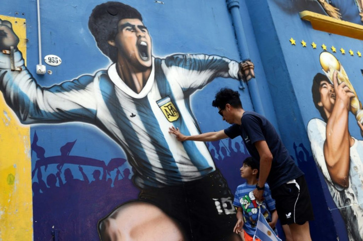 A man and his child pay tribute next to a mural depicting Argentine football legend Diego Maradona  in Buenos Aires on November 25, 2020, on the day of his death