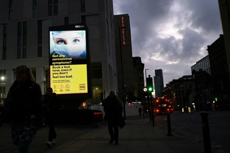 People pass a COVID-19 information sign as they walk in Manchester, northwest England