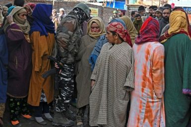 A paramilitary soldier walks next to voters queueing to cast their ballots at a polling station in Indian-administered Kashmir