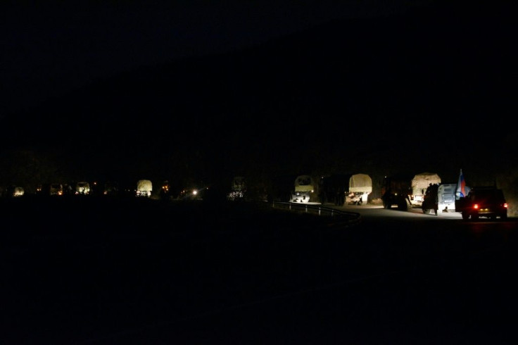 A column of Azerbaijani military trucks flanked by Russian peacekeepers drives along the road near the town of Lachin
