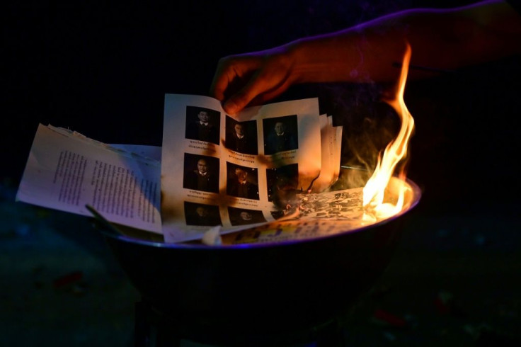 Pro-democracy activist Parit "Penguin" Chiwarak burns pieces of paper featuring headshots of judges on the Constitutional Court