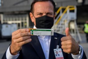 Sao Paulo Governor Joao Doria shows off a package of the CoronaVac vaccine as containers carrying doses of it are unloaded from a cargo plane that arrived from China at Guarulhos International Airport, near Sao Paulo, Brazil