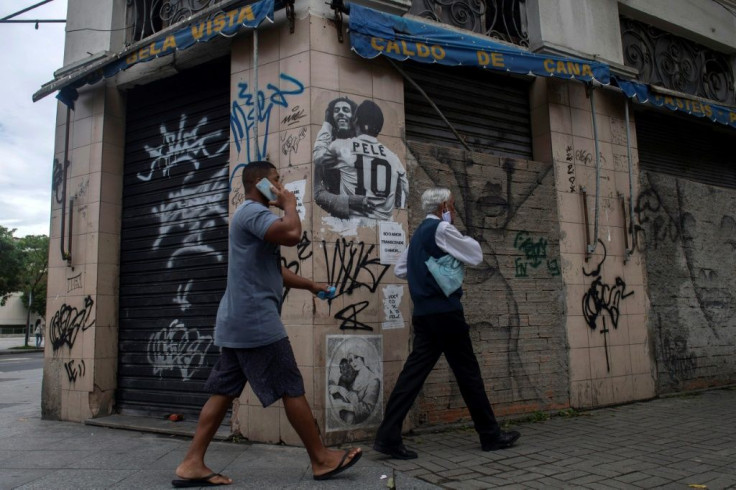 Men walk past a wall of a closed bar with a grafitti of late Jamaican singer Bob Marley and former Brazilian footballer Pele hugging each other in Rio de Janeiro, Brazil, where many stores remain closed due to the coronavirus pandemic, on December 08, 202