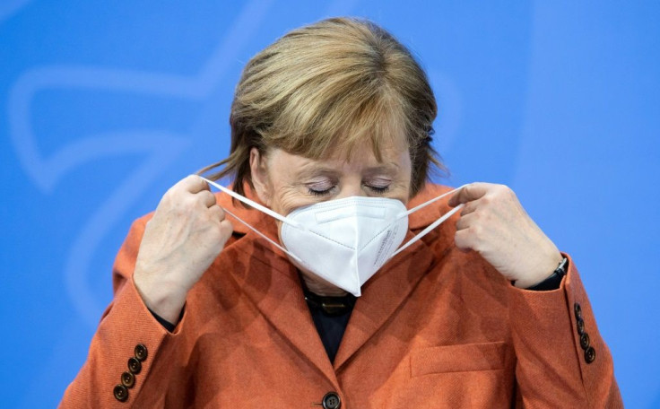 German Chancellor Angela Merkel puts off her face mask before a press conference following crunch talks via video conference with Germany's state premiers on extending coronavirus restrictions